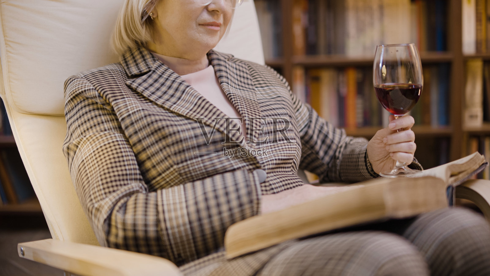 一个成熟的女人在她舒适的家庭图书馆里端着一杯酒看书的特写照片摄影图片
