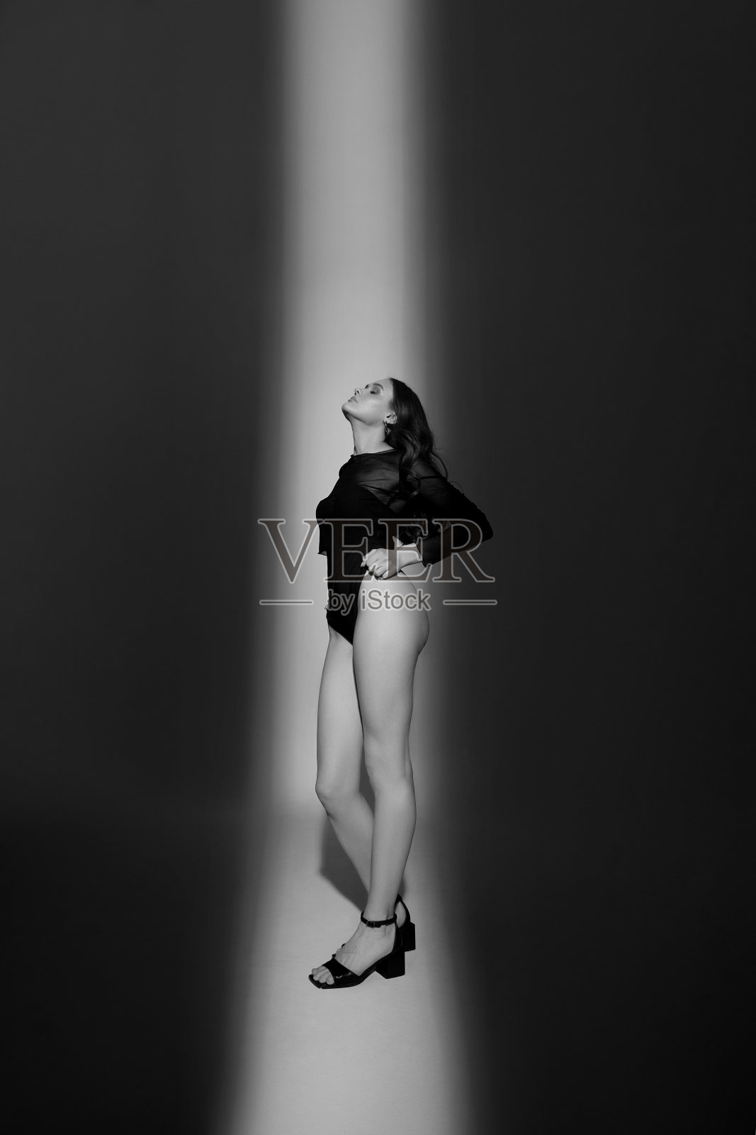 在白色背景的工作室里有着美丽长腿的女人。穿着黑色紧身衣,长卷发的性感年轻女子照片摄影图片