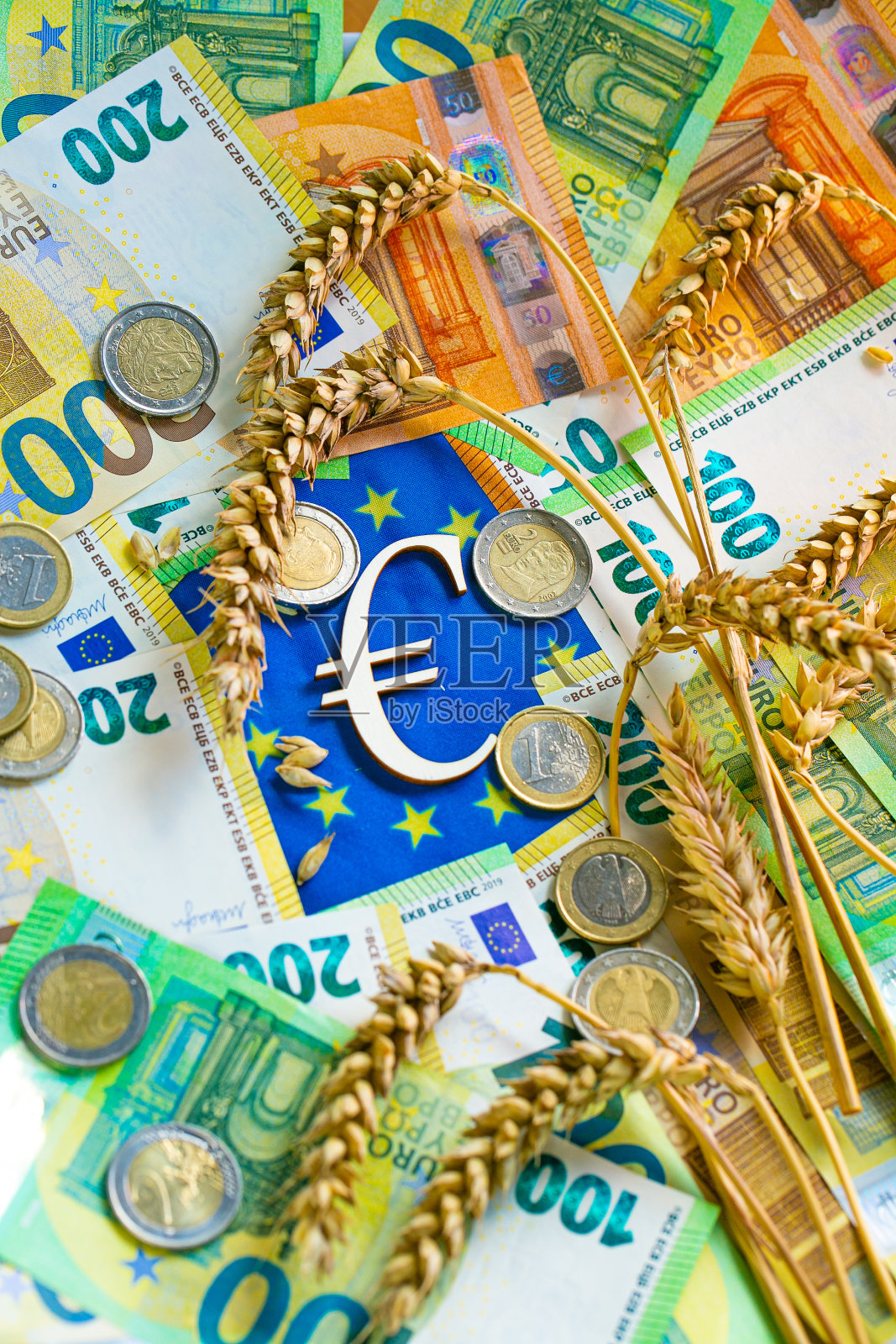小麦在欧盟的价格。欧元硬币和印有欧盟旗帜的谷物。小麦和面粉在欧洲的价格。欧元硬币印在小麦小穗上,欧元纸币印在欧盟旗帜上照片摄影图片