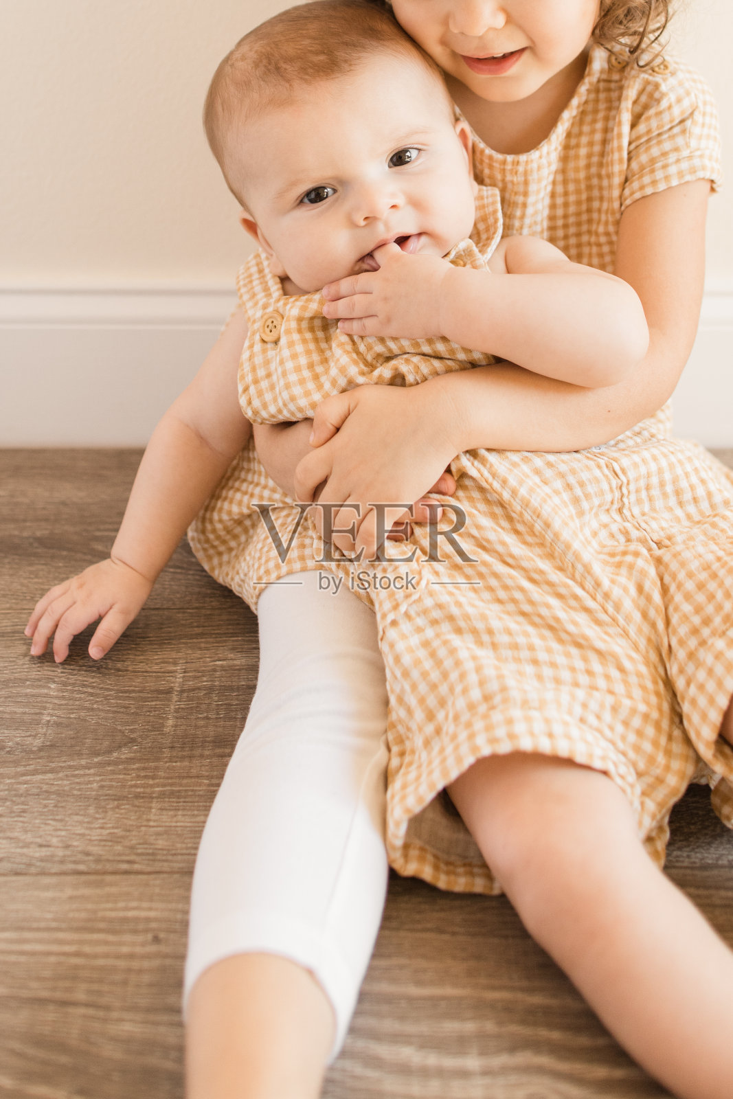 一个3岁的小女孩抱着她5个月大的弟弟,穿着相配的黄色格子衣服,坐在一起照片摄影图片