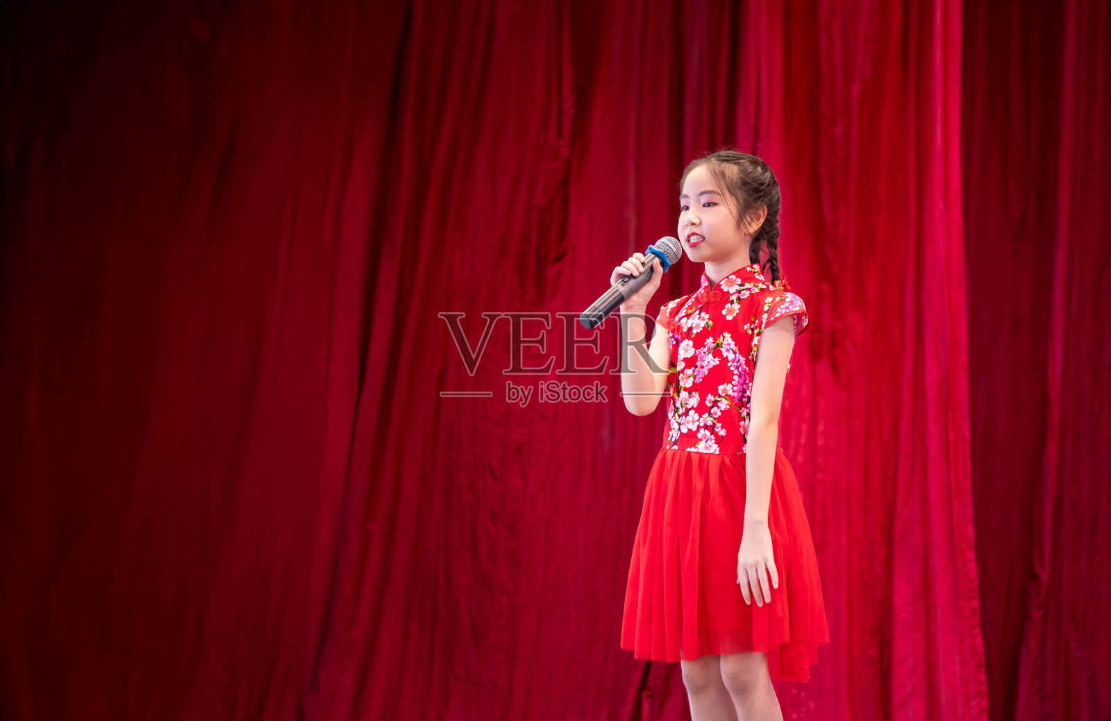 亚洲女孩在学校活动日的舞台上唱歌,穿着旗袍风格,红色窗帘背景照片摄影图片