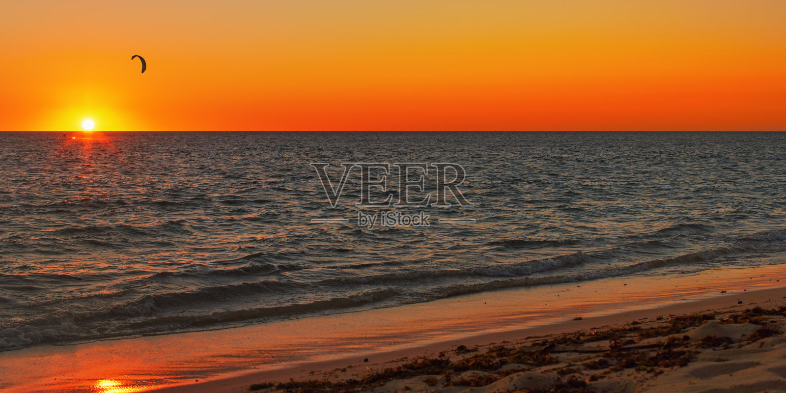 太阳落在平静的海面上,明亮的橘红色的天空,远处风筝冲浪者的剪影照片摄影图片