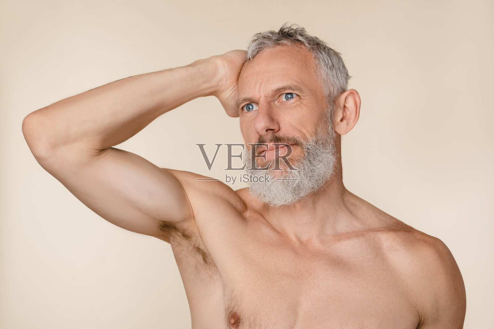 米色背景中是头发和胡子都已花白、肌肉发达、光着膀子的白种中年男子。男性美容的概念照片摄影图片