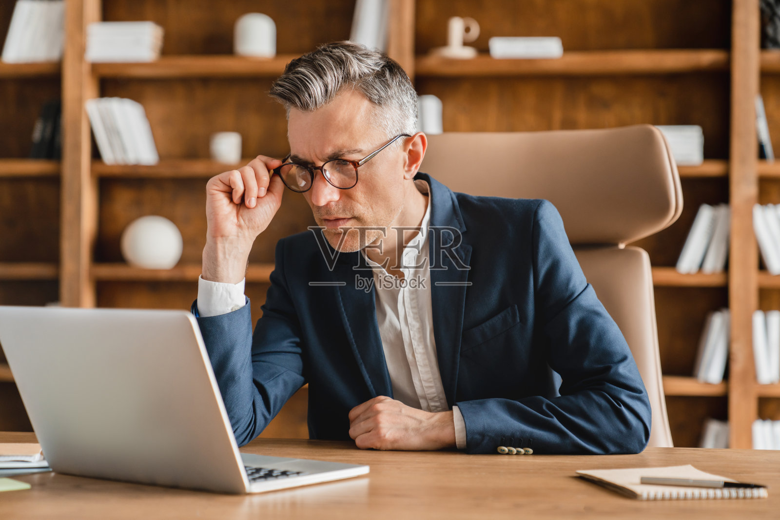 严肃集中的高加索成熟中年商人,ceo,老板,自由职业者,教师,心理学家,穿着正装,西装,工作,在办公室远距离的笔记本电脑上有问题照片摄影图片