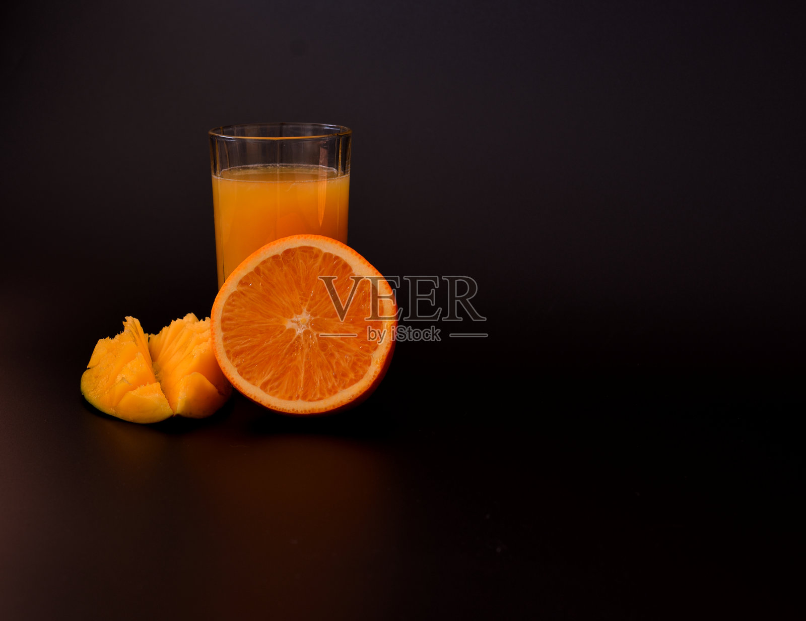 一杯黑色背景的鲜榨果汁,旁边是几片熟芒果和半个橙子。照片摄影图片