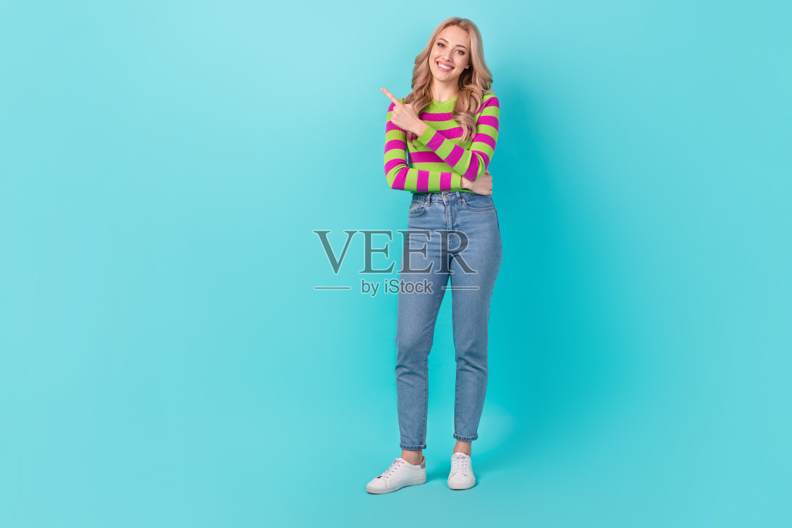 友好甜美的女人穿着条纹毛衣的全长照片指着空白的空间孤立的绿松石色背景照片摄影图片