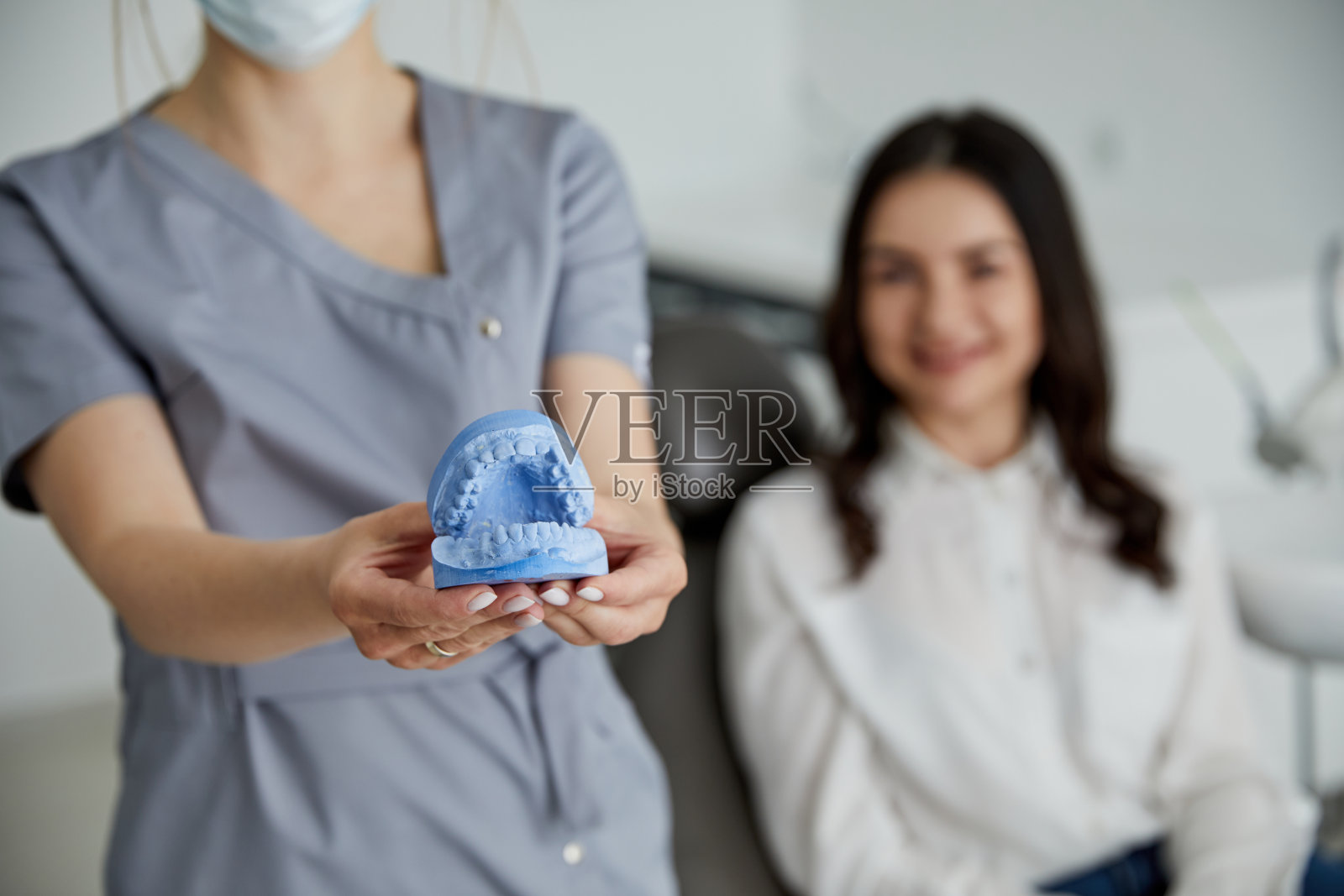 年轻女牙医站在中年成年妇女在诊所的肖像。女牙医在牙科门诊内修复病人的牙齿照片摄影图片