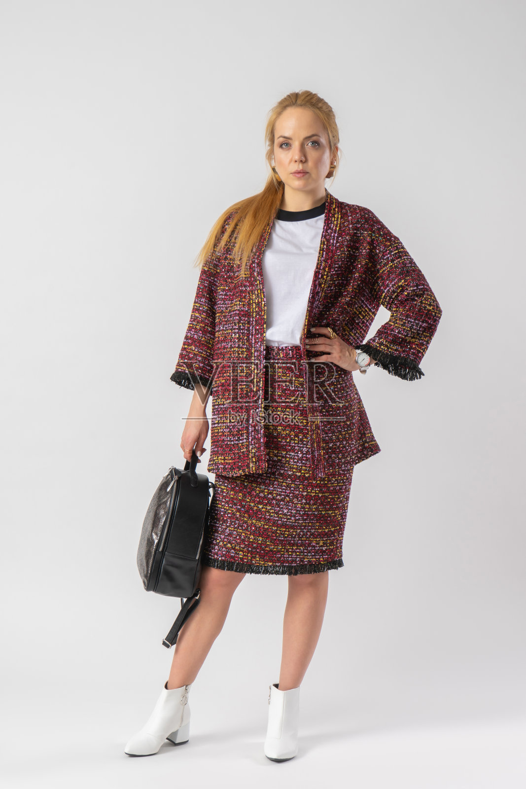 一个年轻的金发女郎,穿着一套休闲温暖的办公室装,手里拿着一个包。照片摄影图片