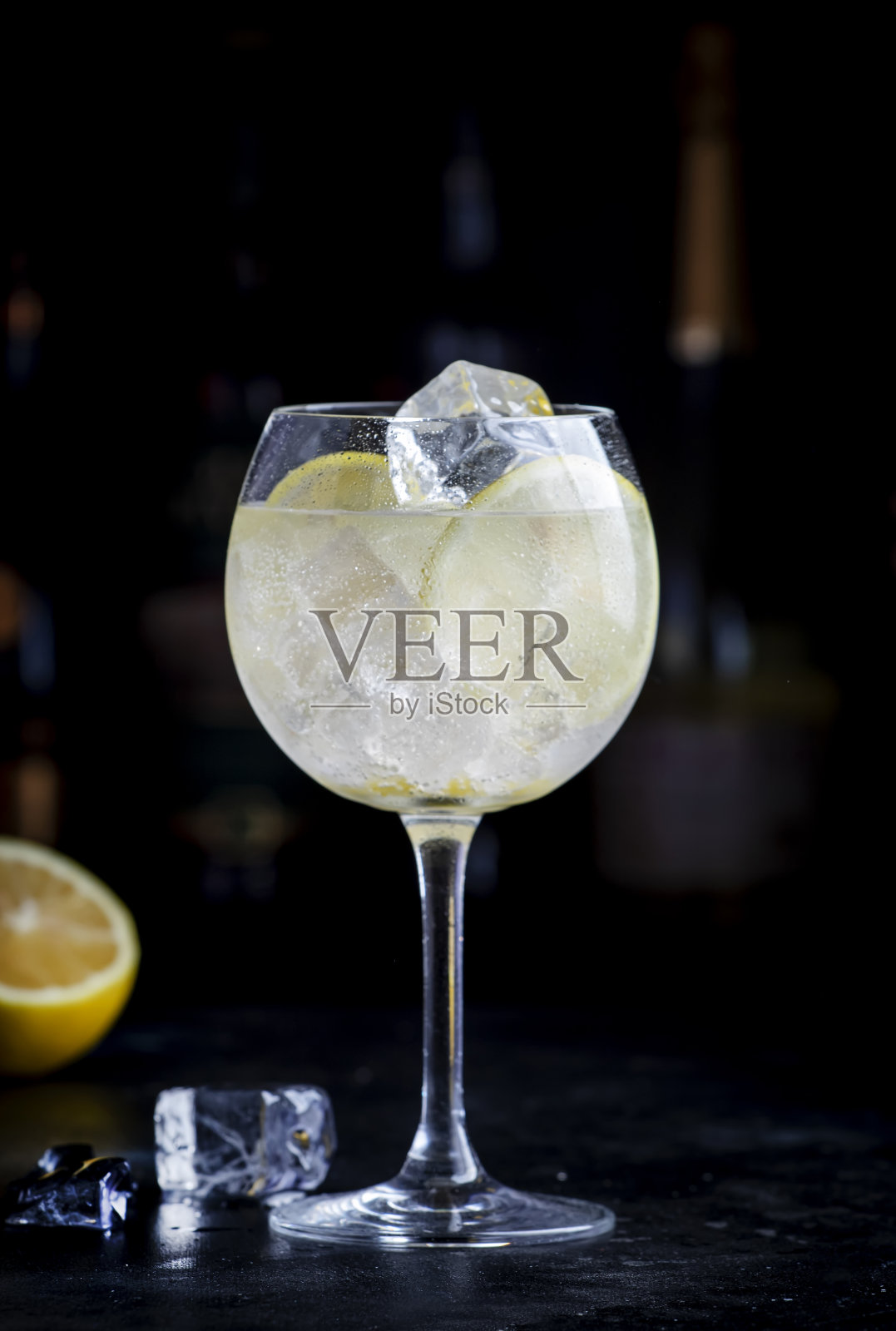 马提尼汤力酒精鸡尾酒,加入白苦艾酒、汤力、柠檬和冰块。黑色吧台背景,钢制工具和瓶子照片摄影图片