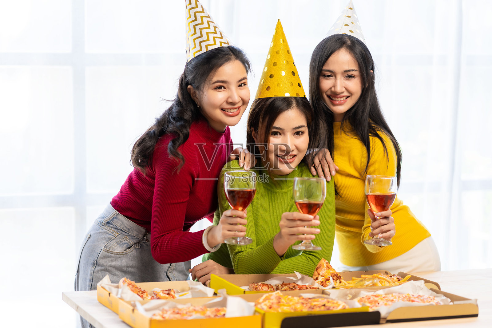 三个戴着派对帽的漂亮女孩正兴高采烈地用五颜六色的上衣庆祝她们的生日。快乐的亚洲商业团体在办公室喝香槟照片摄影图片