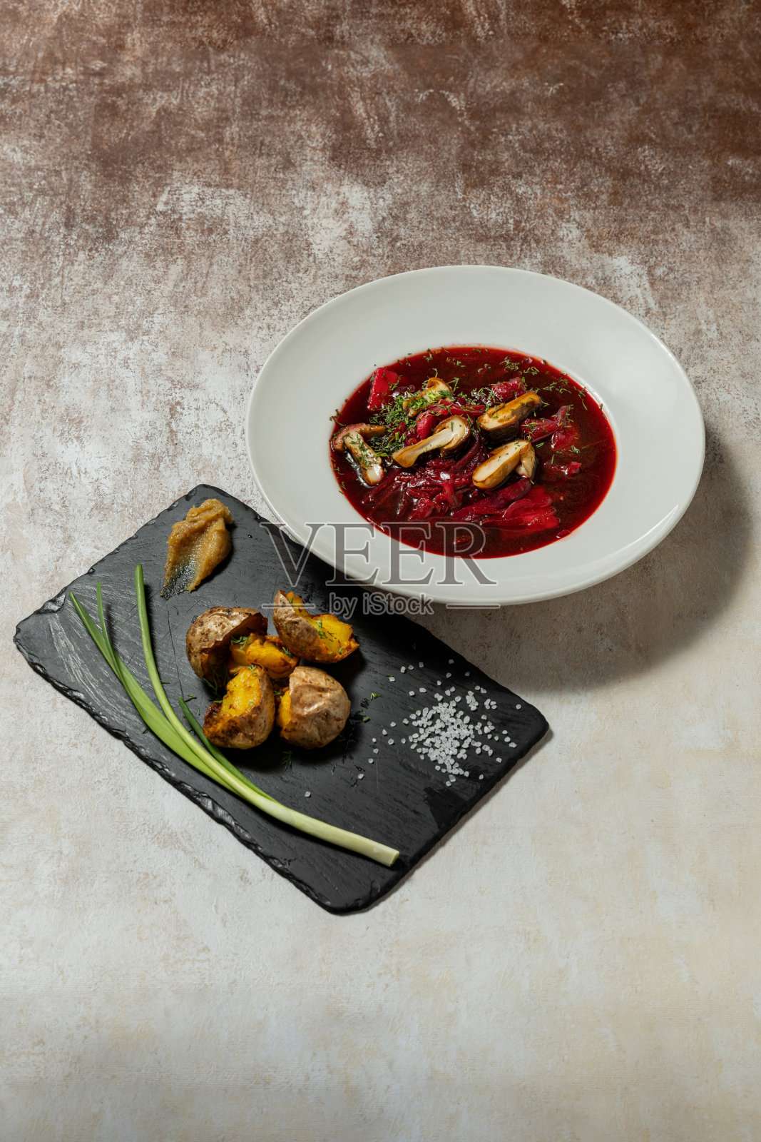 乌克兰禁食汤罗宋汤,在一个轻陶瓷盘子里放上蘑菇和蔬菜。旁边是一个石板盘子,上面放着炸土豆和葱。盘子放在浅色的织物背景上。照片摄影图片