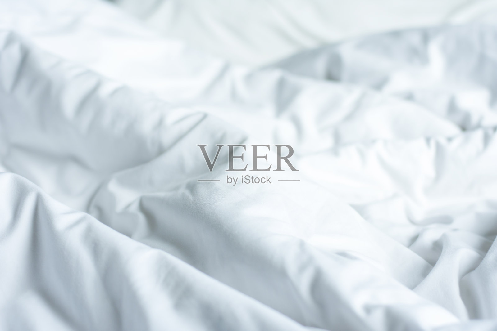 在一个漫长的夜晚醒来后,褶皱凌乱的卧室毯子,羽绒被和毯子的细节,一个未整理的床在酒店卧室的白色毯子。照片摄影图片