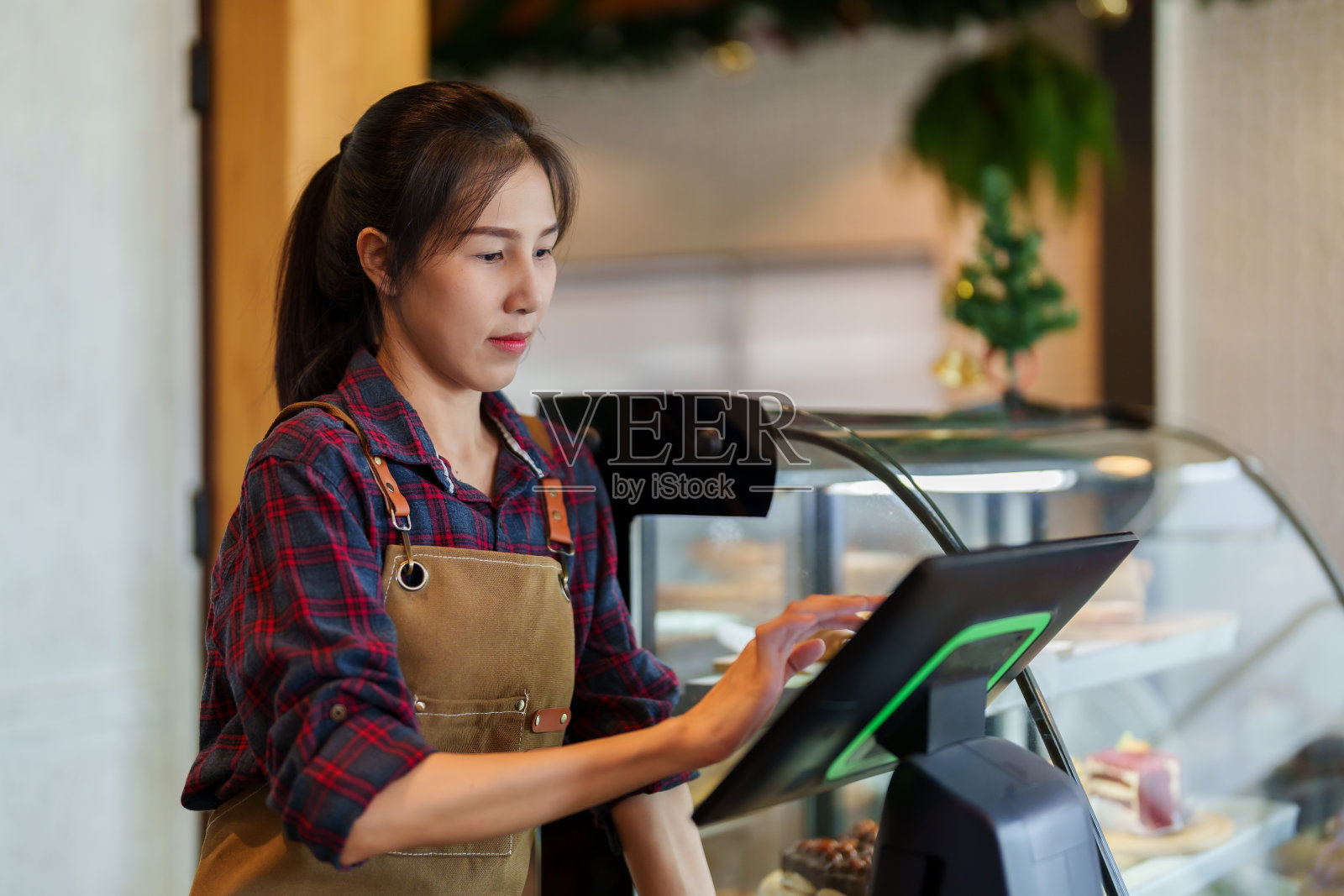 美丽的亚洲烘焙咖啡馆的老板。站在商店的柜台后面,在商店的收银机前收钱。可以在前台点餐的机器。专注于机器照片摄影图片