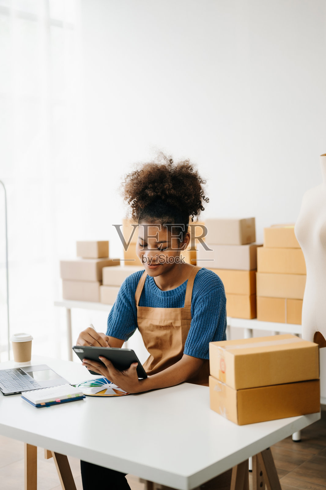 创业小型企业中小企业,企业家老板非洲妇女使用智能手机或平板电脑接收和检查网上购物订单,准备包装产品盒。在办公室照片摄影图片