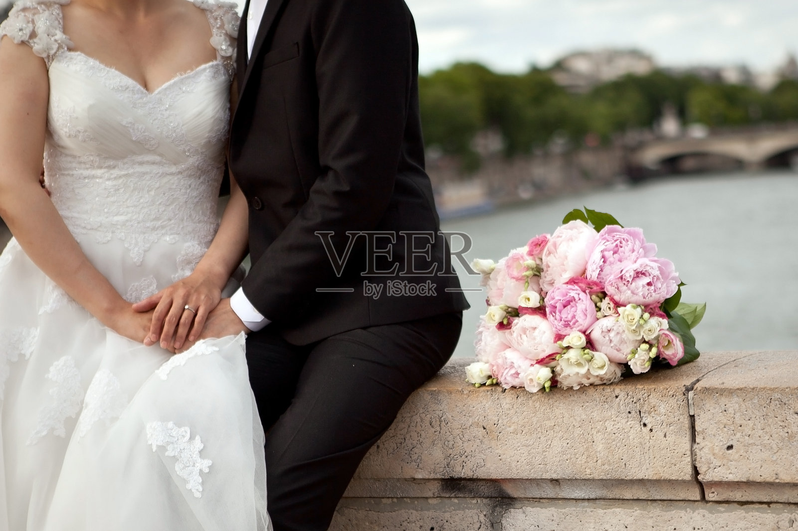新娘和新郎坐在桥的栏杆上,背景是新娘的婚礼花束照片摄影图片