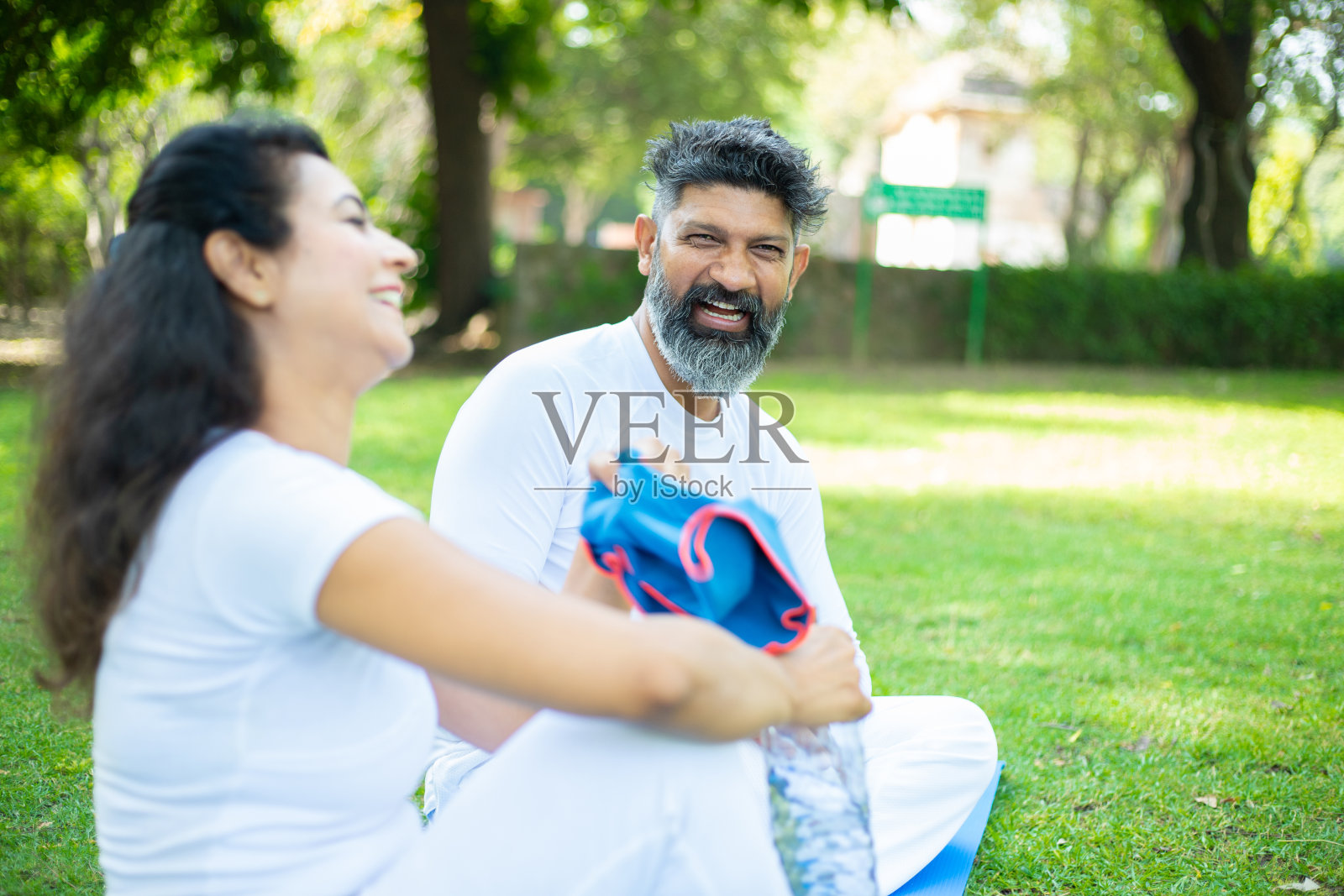 印度男人和女人在瑜伽锻炼后坐在公园里放松和大笑,亚洲夫妇在户外花园一起度过愉快的时光。有选择性的重点照片摄影图片