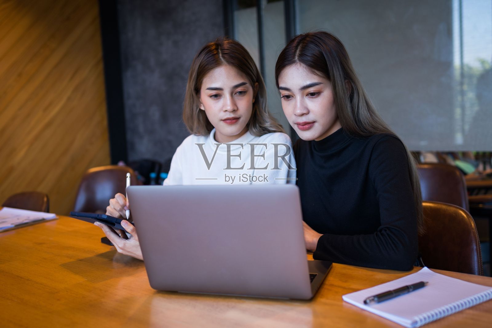 两位女性专业人士在现代办公室里用笔记本电脑工作照片摄影图片