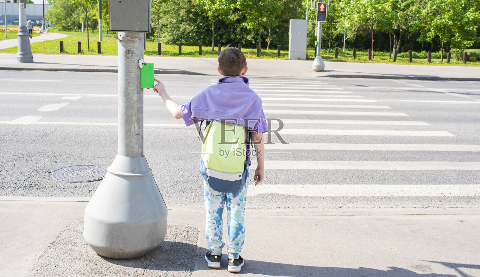 男孩按下交通灯按钮,站在人行横道前,准备过马路照片摄影图片