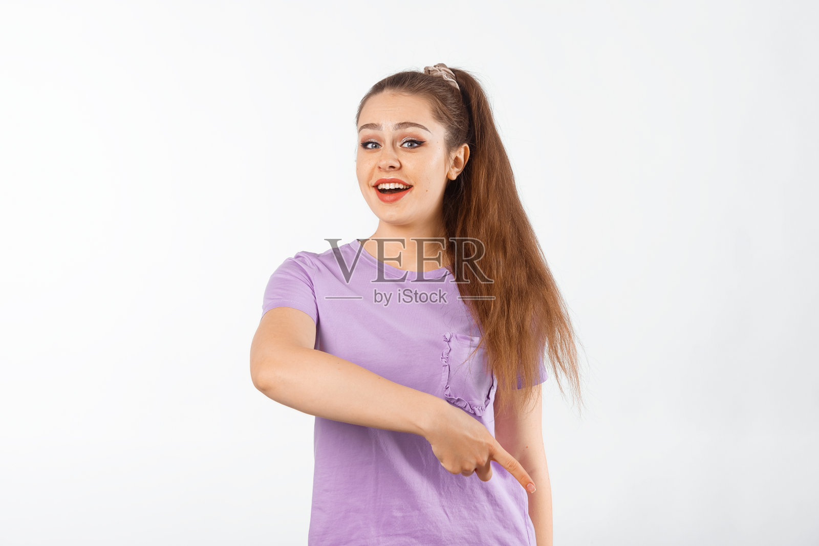 快乐的年轻女子,一头长发,手指向下,微笑着,展示着广告,下面的产品,促销报价,穿着休闲t恤站在白色背景上照片摄影图片