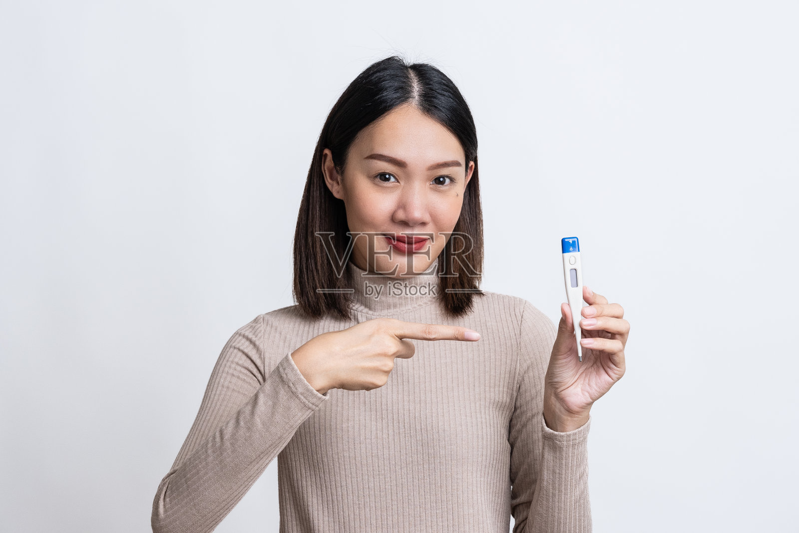 美丽快乐的年轻亚洲女子的肖像在孤立的白色背景上,拿着温度计,感冒后感觉好多了,拇指向上,对着镜头微笑,发烧退了,体温正常。照片摄影图片