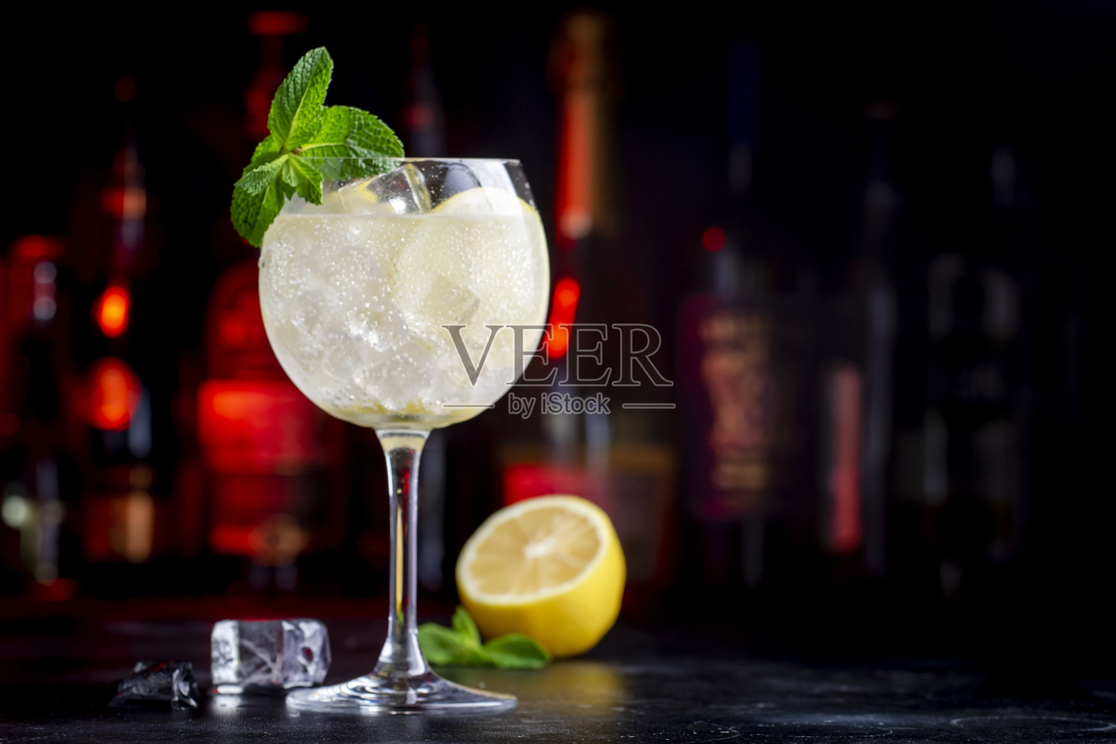 马提尼汤力酒精鸡尾酒,加入白苦艾酒、汤力、柠檬、薄荷和冰块。黑色吧台背景,钢制工具和瓶子照片摄影图片