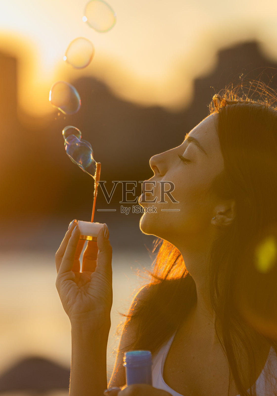 夕阳下,年轻女子在玩泡泡棒。照片摄影图片