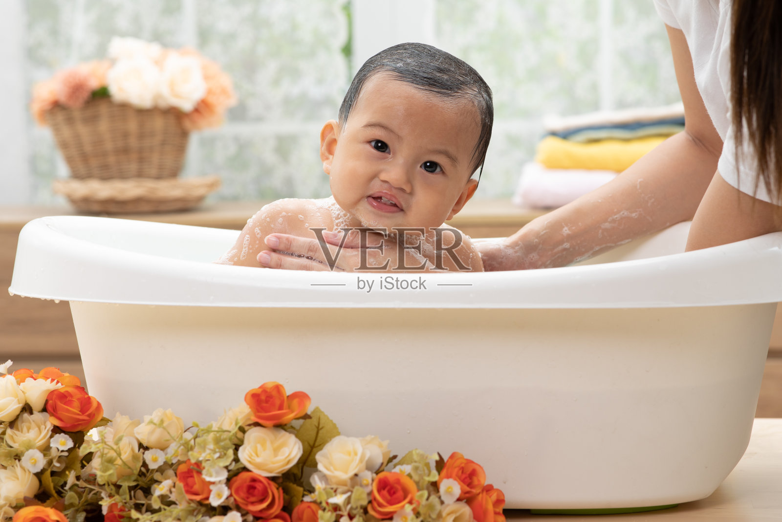 可爱的亚洲新生婴儿在浴缸里洗澡。母亲用温水给儿子洗澡。快乐可爱的新生婴儿在浴缸里微笑,放松和舒适。新生儿护理理念照片摄影图片