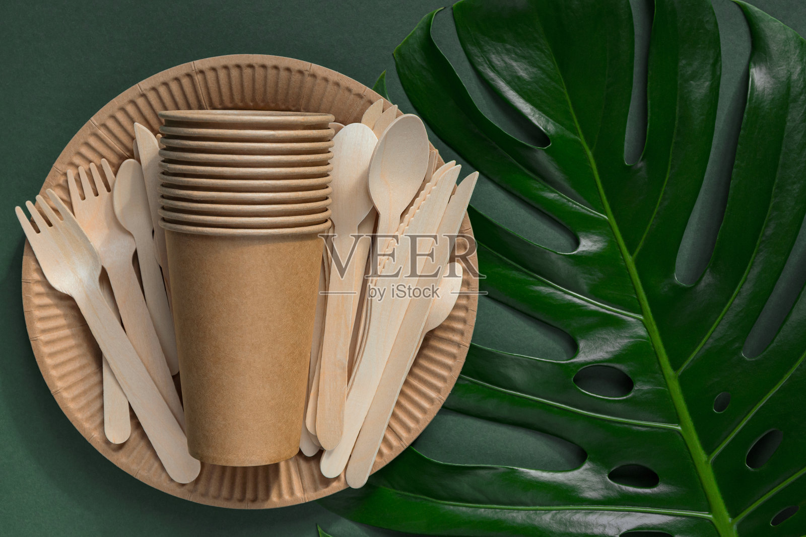 生态友好的牛皮纸餐具在绿色背景与monstera叶。回收的概念。前视图。平的。“零浪费”的主题照片摄影图片