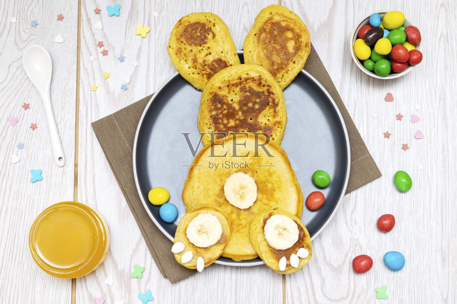 复活节有趣的创意健康早餐午餐食品的创意,儿童。兔子,兔子煎饼,香蕉与蜂蜜,甜甜的糖果,鸡蛋盘子木桌背景。俯视图平铺照片摄影图片