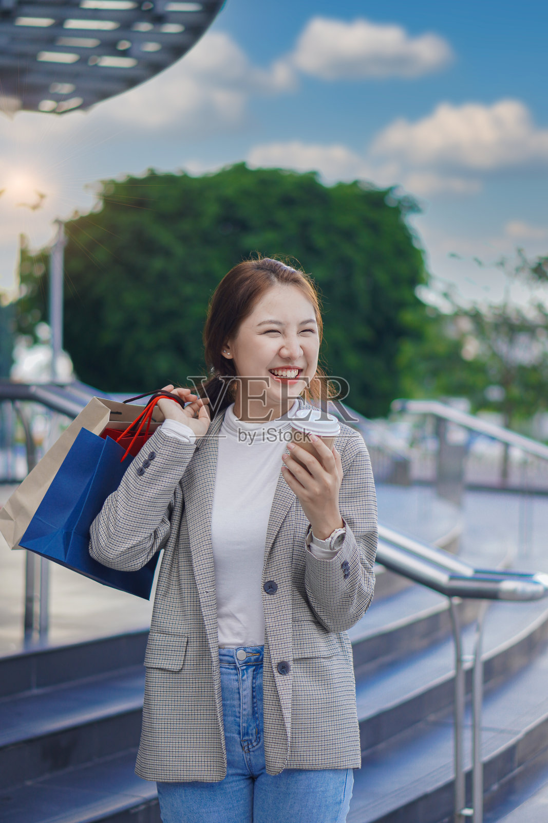 拿着彩色购物袋的亚洲女性在购物中心前开心地笑着。照片摄影图片