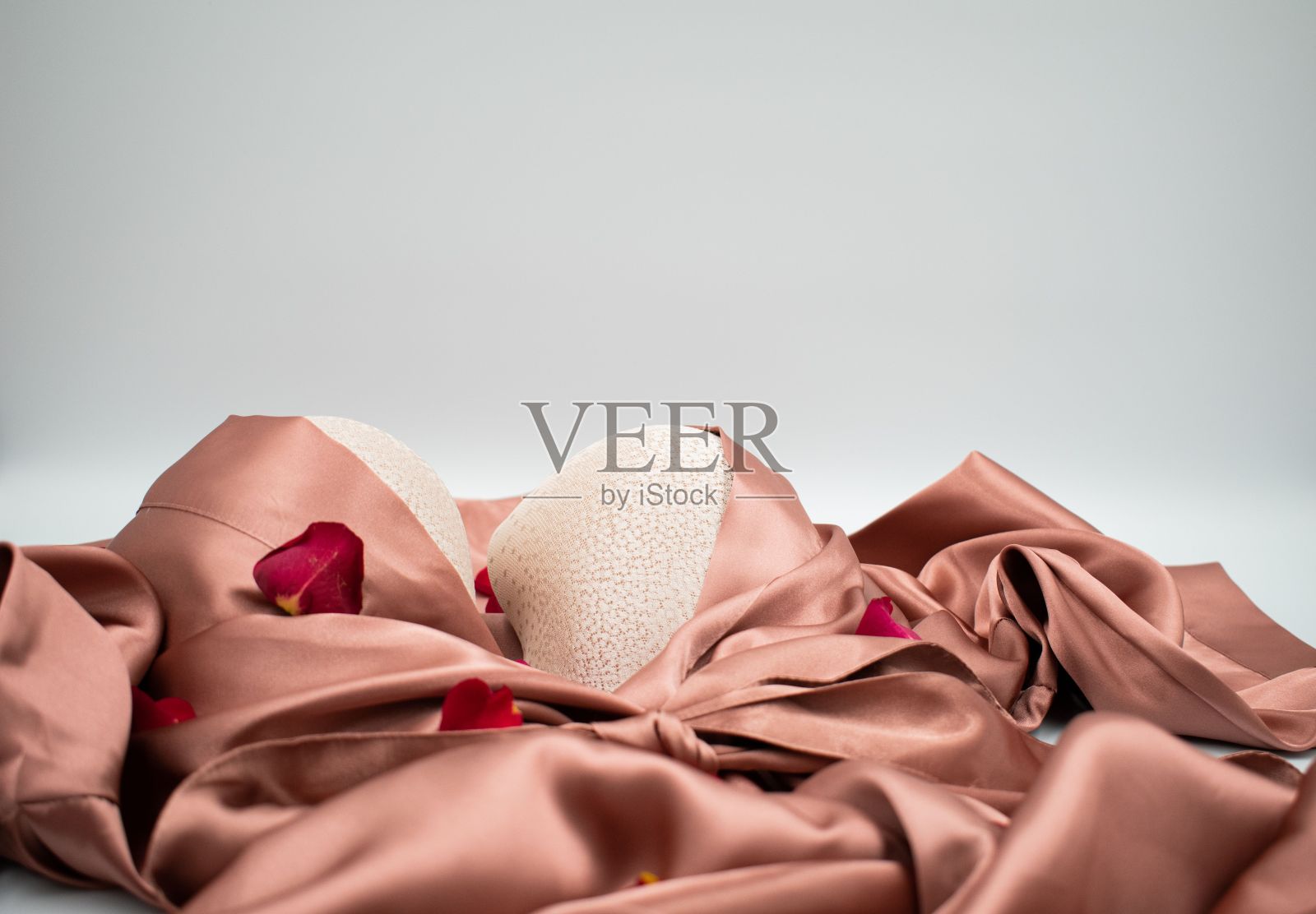 粉色缎子长袍和白色表面有玫瑰花瓣的胸罩照片摄影图片