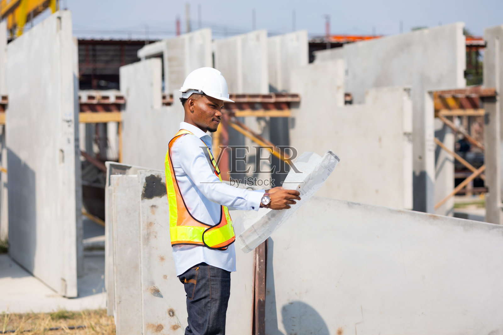 年轻的非裔美国建筑师戴着安全帽的工程师在工厂的工业设施里看蓝图。重工业制造厂。预制混凝土墙照片摄影图片