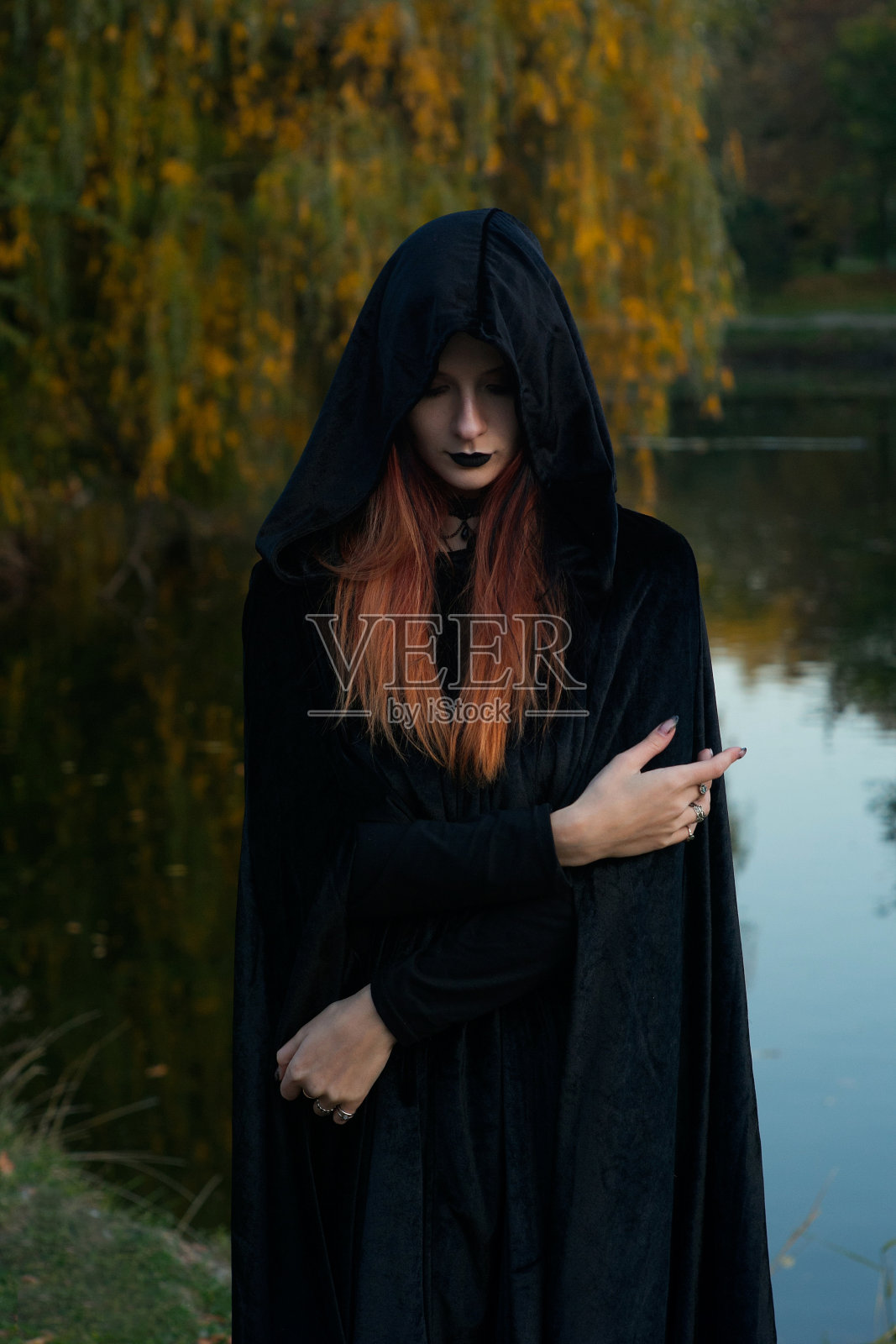 美丽时尚的年轻女孩女巫模特站在秋天的河边的森林里,苍白,吸血鬼,哥特照片摄影图片