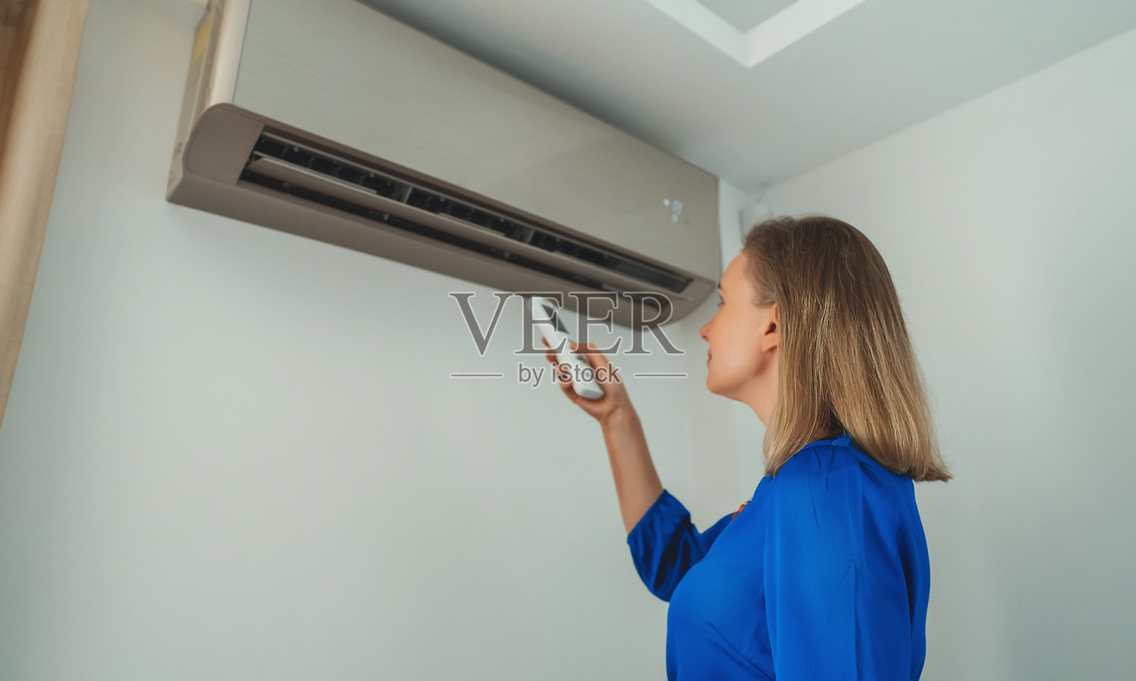 拿着遥控器的女人瞄准了空调。照片摄影图片