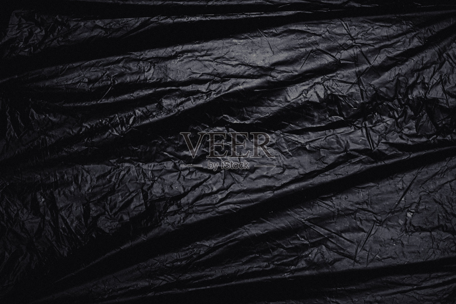 黑色背景上的透明拉伸塑料膜。逼真的保鲜膜纹理叠加和效果。褶皱塑料图案的创意和装饰设计。照片摄影图片