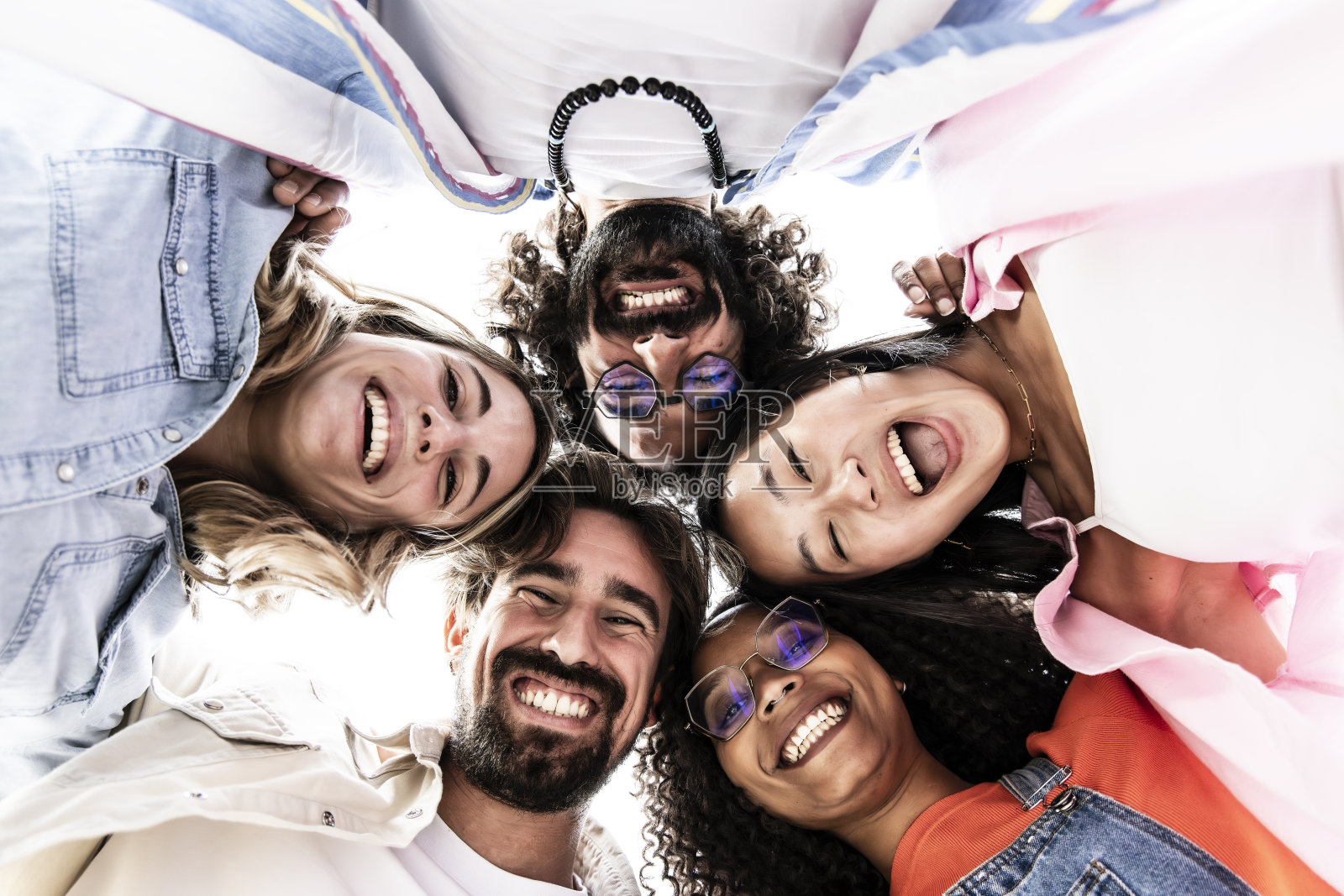 低视角,一群多种族的年轻人站成一圈,笑着盯着镜头。各种快乐的千禧一代围成一圈向下看,玩得开心。照片摄影图片