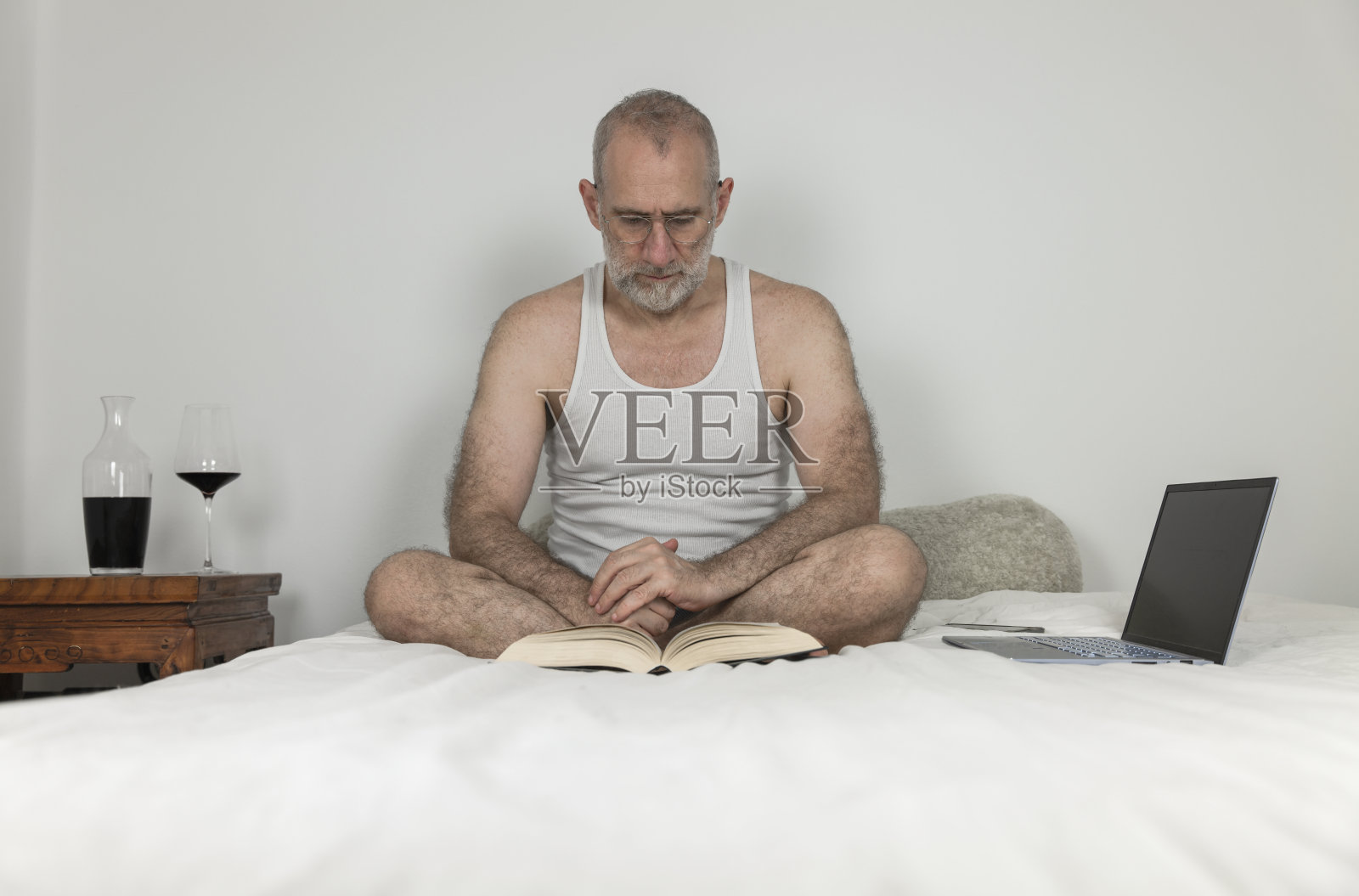 成年男子躺在床上看书,前面放着笔记本电脑照片摄影图片