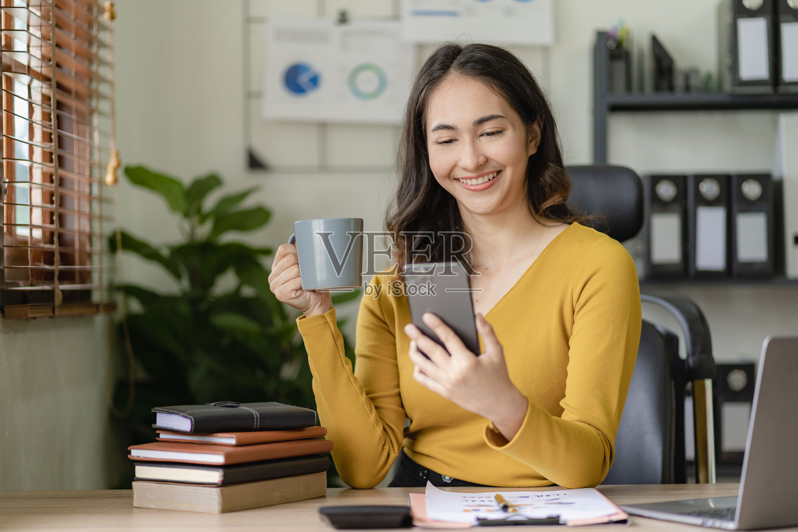 亚洲女商人用智能手机和商业客户聊天,在办公室用笔记本电脑做数学,学习税务、会计、金融概念照片摄影图片