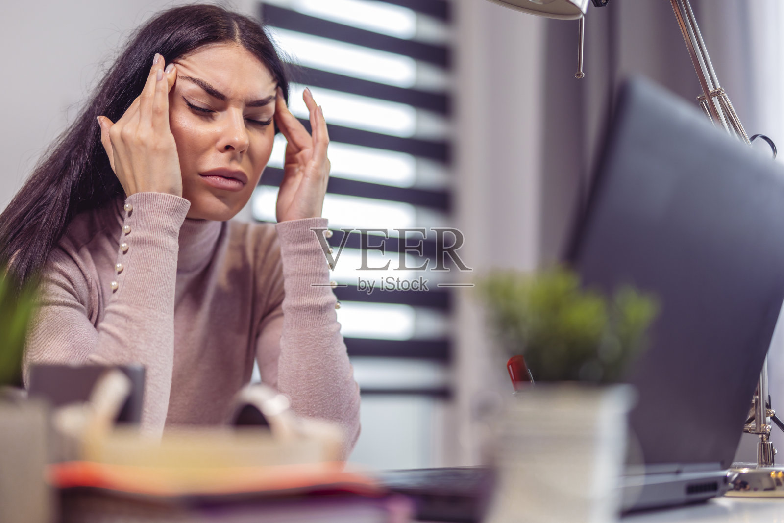 因慢性头痛在办公桌前工作的年轻女子照片摄影图片