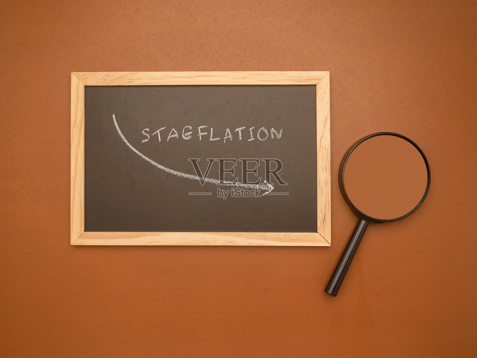 Hand用粉笔在黑板和放大镜上画了一个滞胀箭头,背景是棕色的照片摄影图片