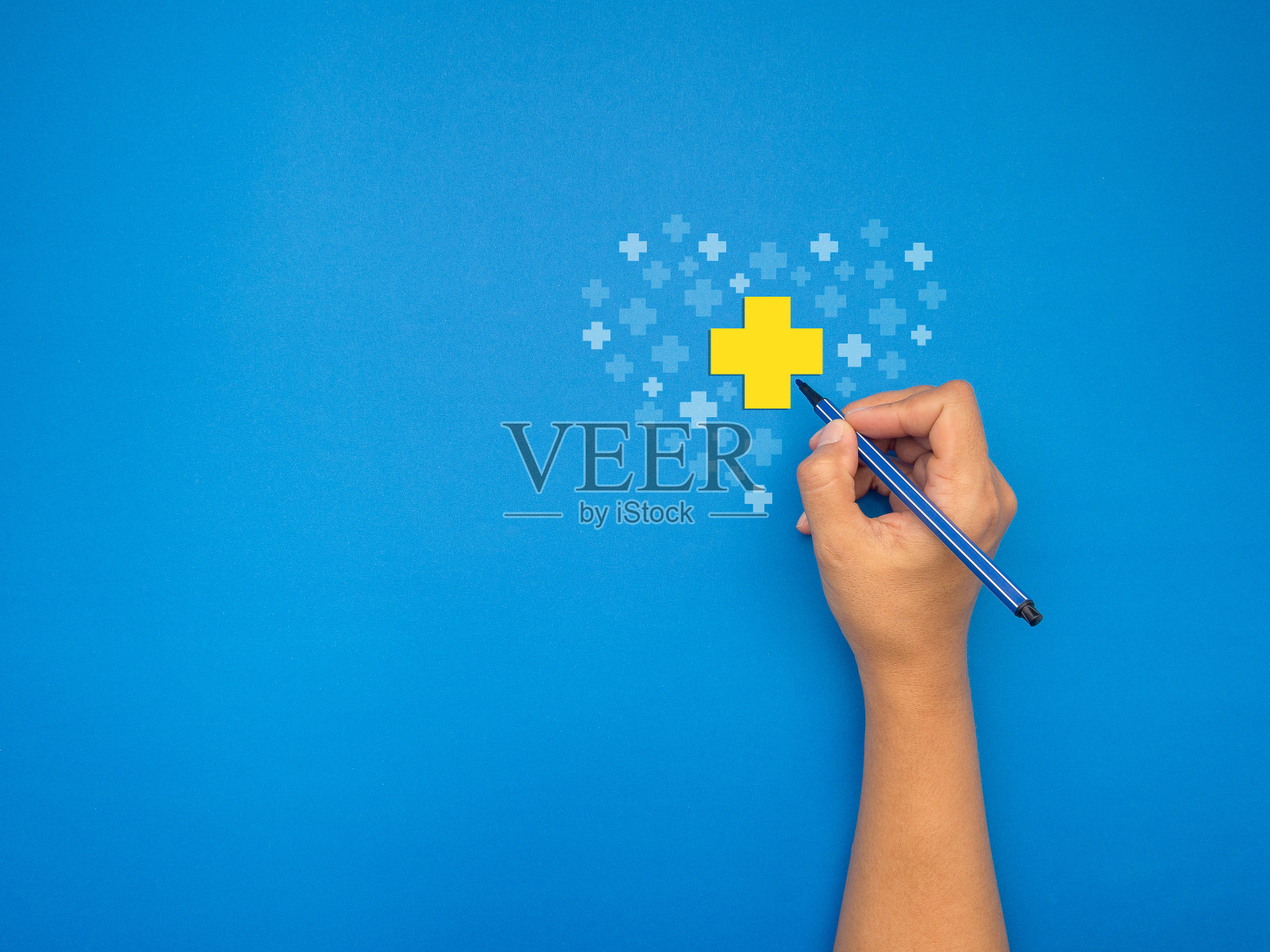 手里拿着一支笔,在蓝色的背景上画着一个黄白相间的十字照片摄影图片