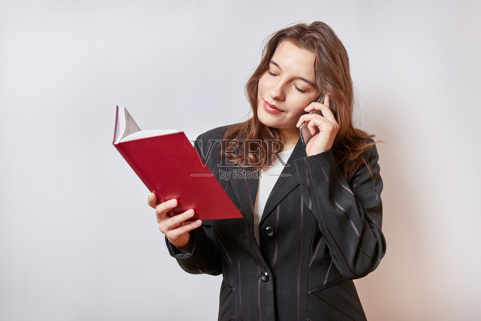 漂亮的女商人一边打电话一边看笔记本上的笔记。照片摄影图片