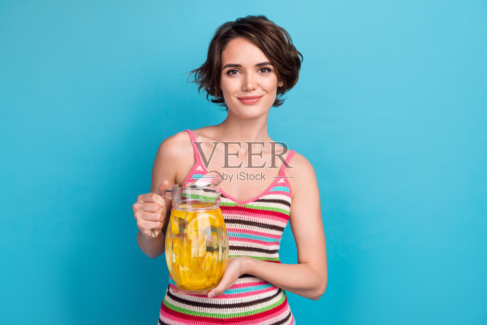 年轻满意的女孩夏天的照片拿着壶杯橙汁柠檬水喝新鲜饮料孤立的蓝色背景照片摄影图片