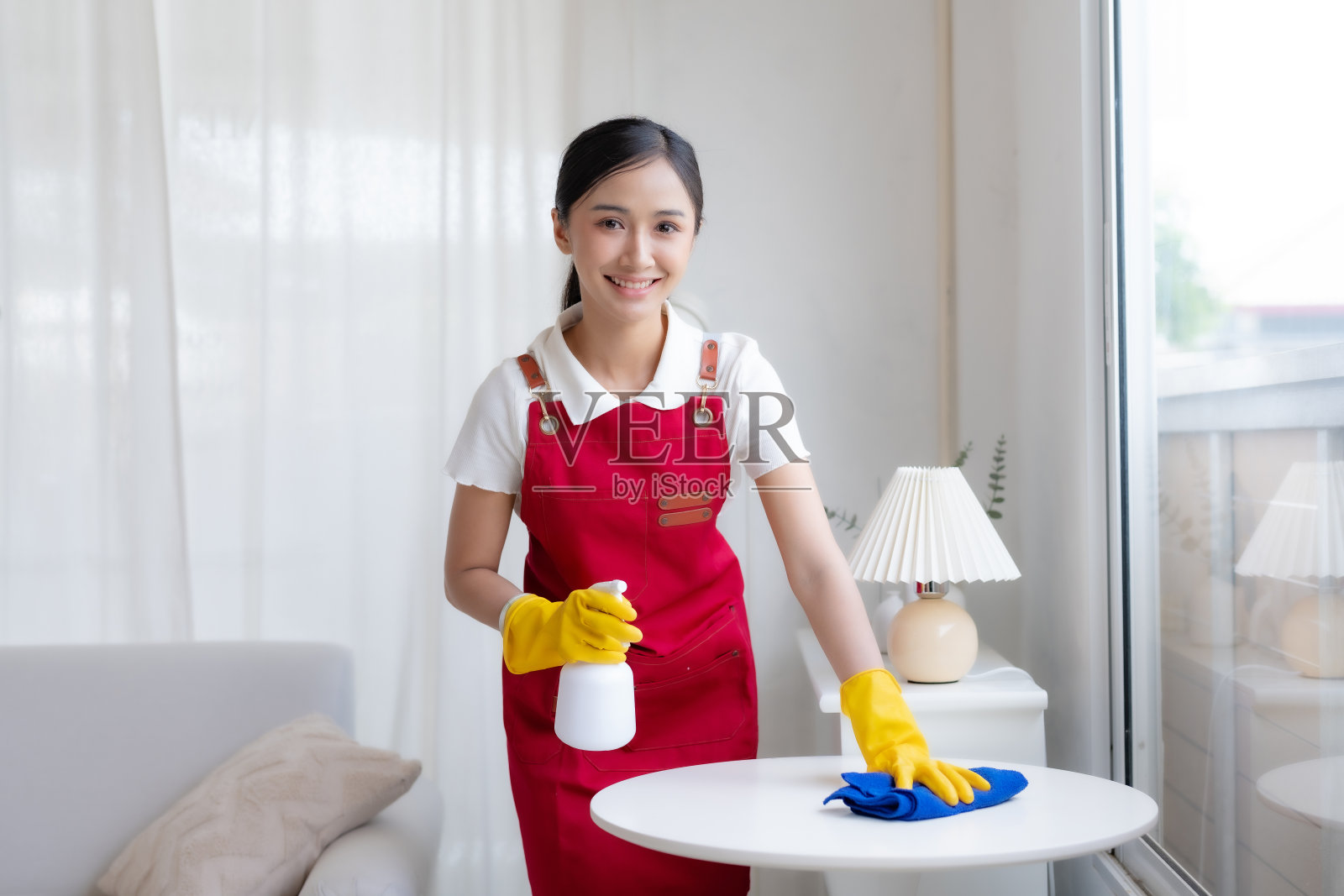 戴着手套、系着围裙的亚洲主妇正在愉快地打扫房间。快乐的亚洲年轻女子正在拖地。照片摄影图片