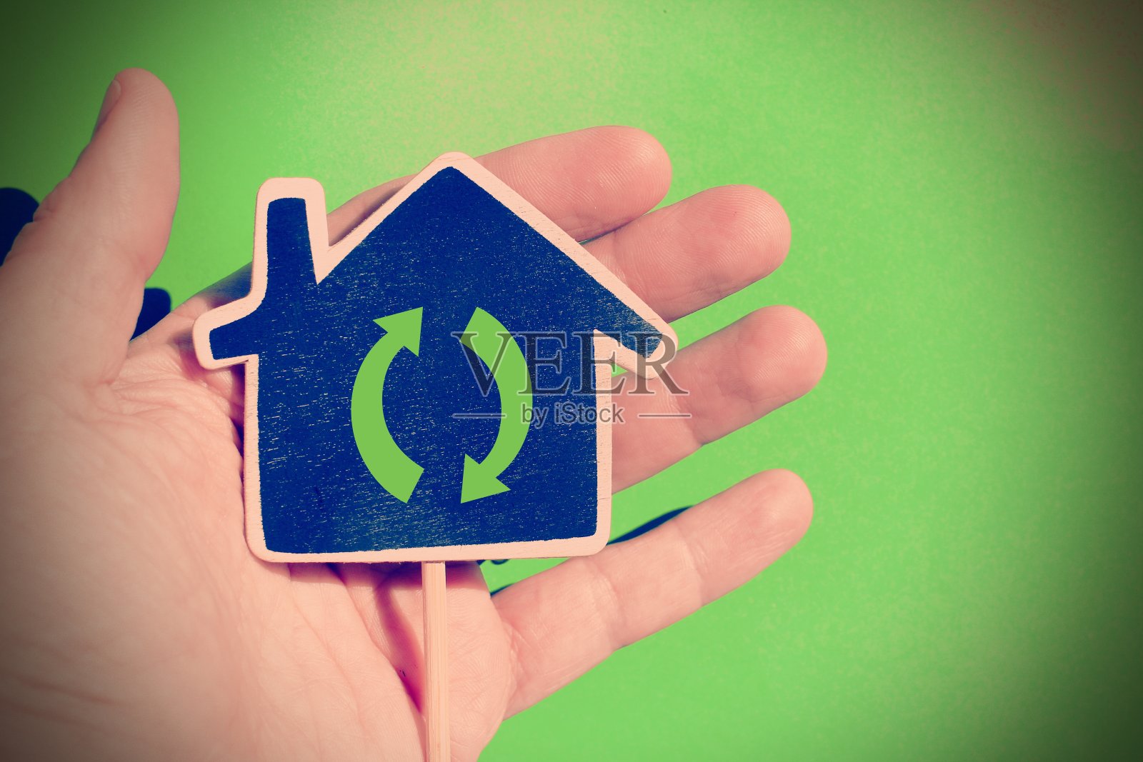 在绿色背景中,手拿着一个标有“回收”字样的房子。照片摄影图片