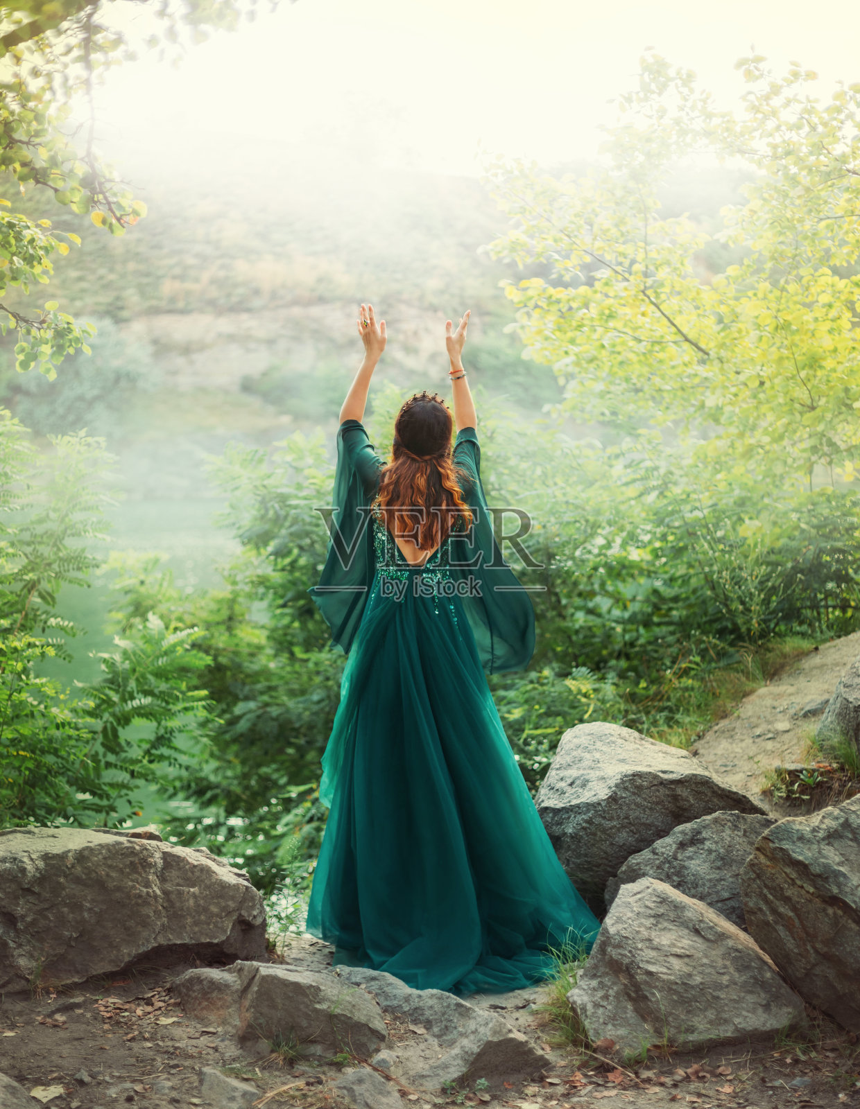 幻想中的红发女女王在夏日森林里向天空举手祈祷。女孩穿着优雅的皇家复古精灵绿色长裙。宽长袖绸在风中飞舞。艺术照片裸露开背。照片摄影图片