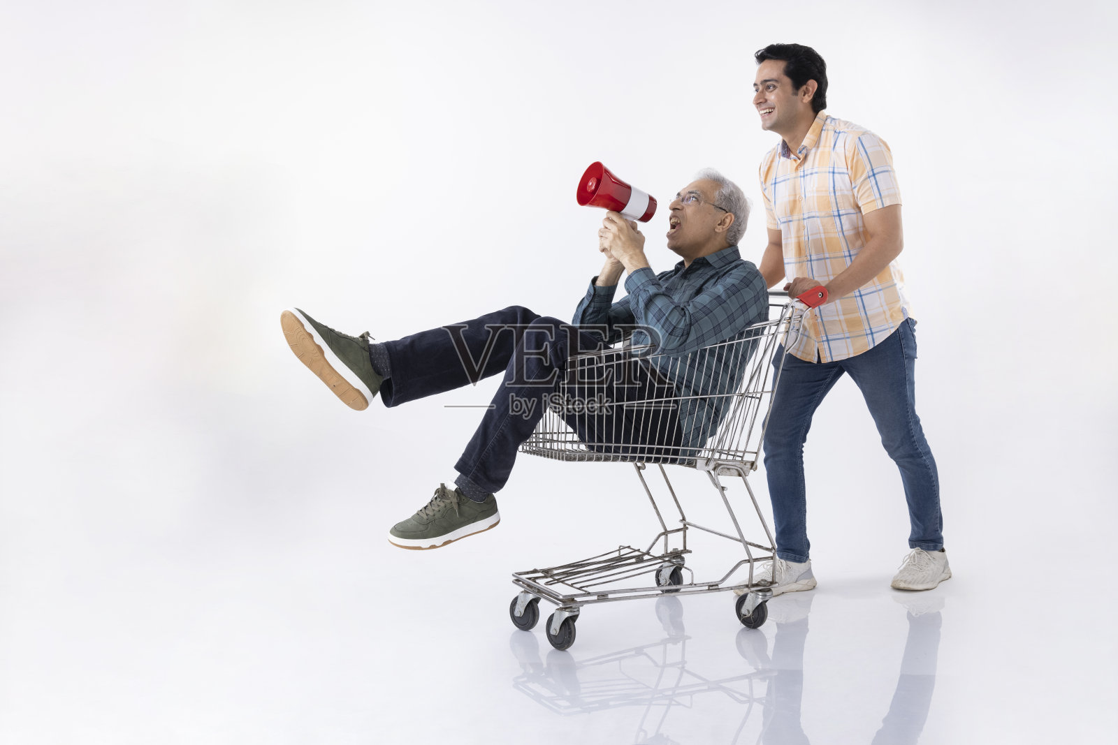 坐在购物车里拿着扩音器的老人和推着购物车的年轻人被隔离在白色背景中。照片摄影图片