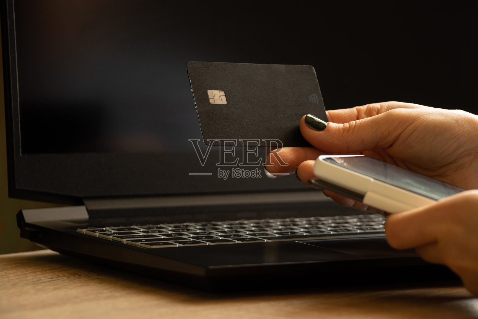 在办公室窗口附近,手持信用卡在黑色笔记本电脑旁进行在线支付的女孩照片摄影图片