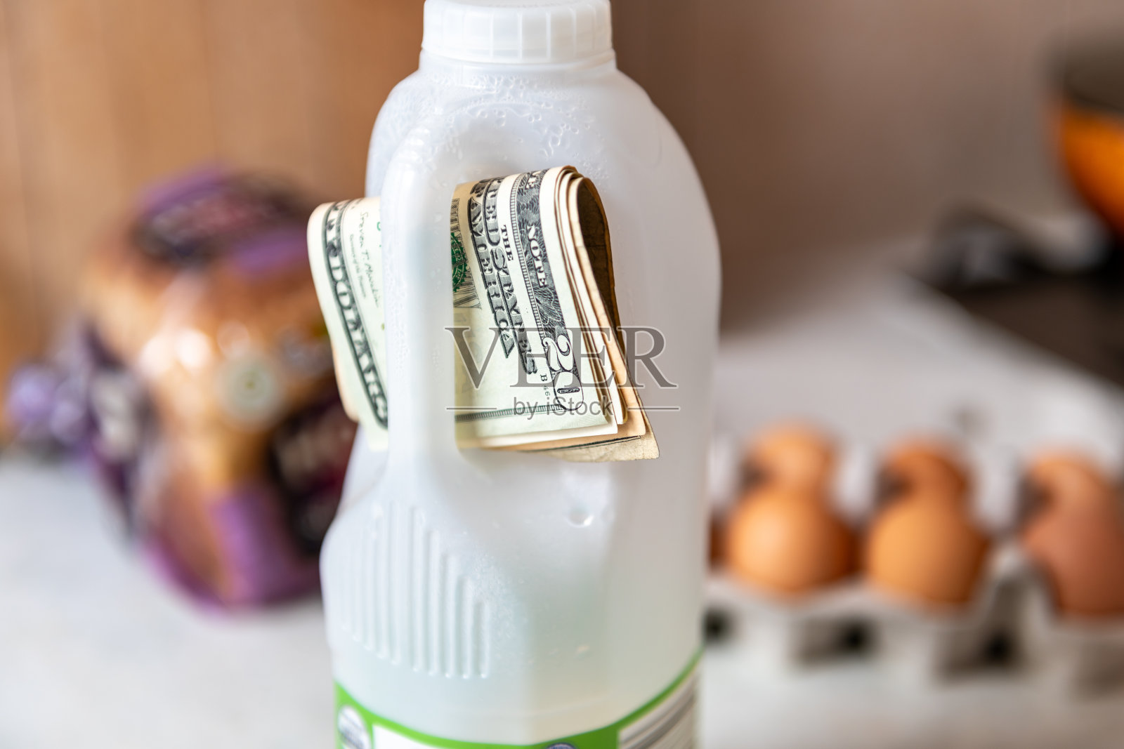 一个生活成本,食品通胀的概念与一捆美元钞票塞在一瓶牛奶的手柄。照片摄影图片