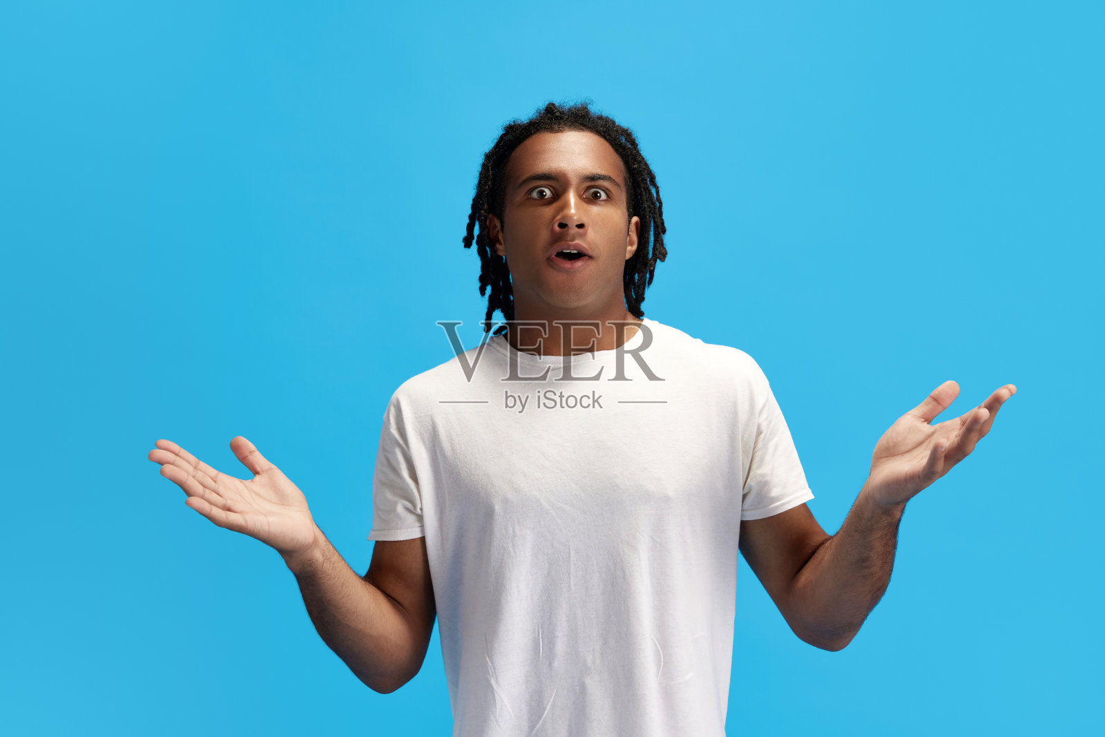 年轻的非洲男子惊恐地张开双手,站在蓝色画室的背景下,脸上露出震惊和惊讶的表情照片摄影图片